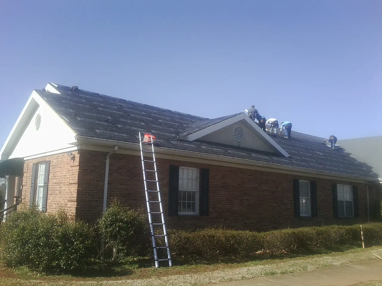 Crew tearing shingles off a brick ranch roof with a ladder set — Emergency Roof Repair work by our crew in Deer Island