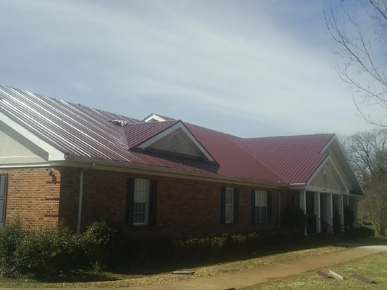 Red metal roof with gabled entries on a long brick building, from a Hail Damage Roof Repair job in Deer Island