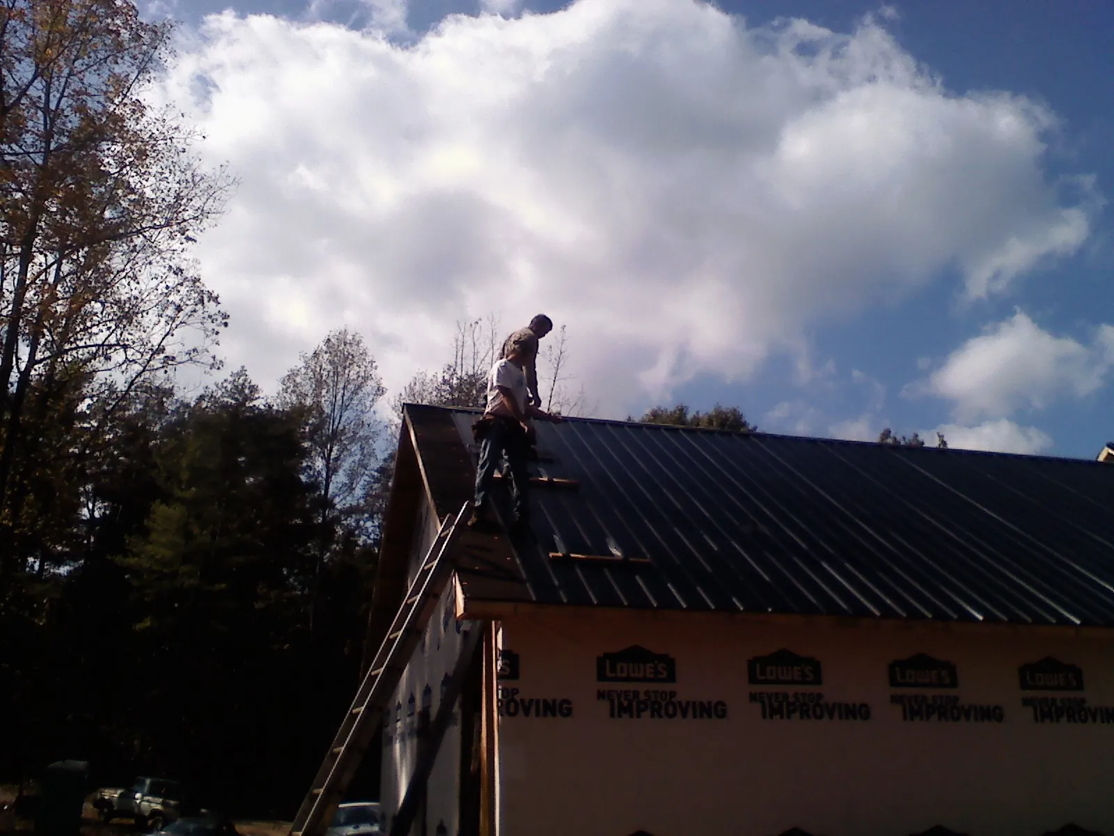 Roofer fastening dark metal panels high against a cloudy sky, from a Roof Inspection job in Deer Island