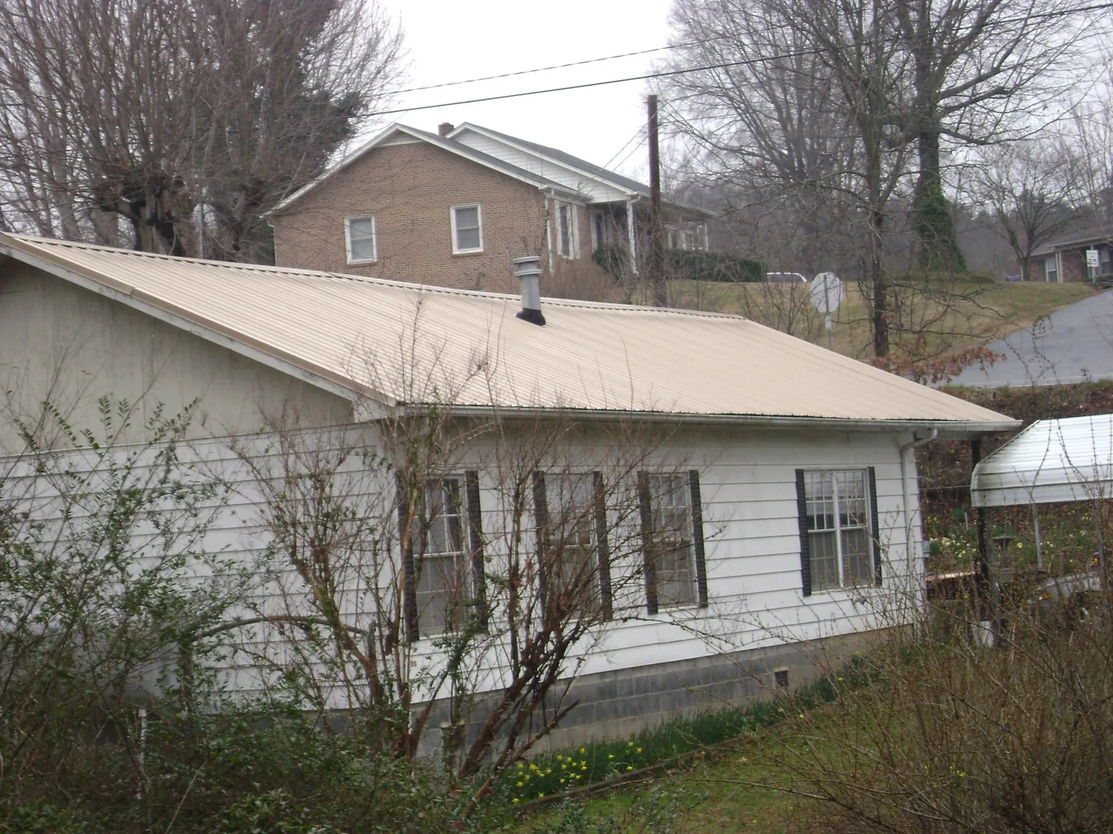 Tan metal roof on a white sided house set into a hillside — Commercial Roofing by Roofing Brothers in Deer Island